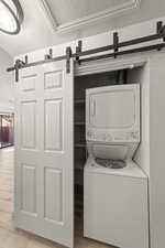 Laundry area with a barn door, a textured ceiling, stacked washer and clothes dryer, and light wood-style flooring