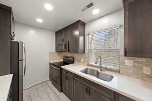 Kitchen with dark wood finish cabinetry, stainless steel appliances, light stone countertops, backsplash, and wood tiled floors