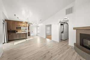 Unfurnished living room featuring lofted ceiling, hanging lights, light wood-style flooring, a glass covered fireplace, and a barn door