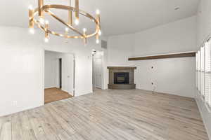 Unfurnished living room with light wood finished floors, suspended lighting, and a fireplace with raised hearth
