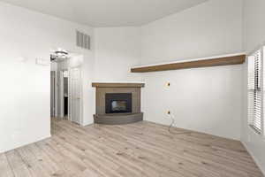 Unfurnished living room featuring light wood-type flooring, a glass covered fireplace, and a high ceiling