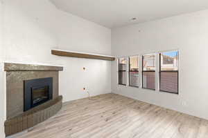 Unfurnished living room featuring light wood finished floors, a glass covered fireplace, and a high ceiling