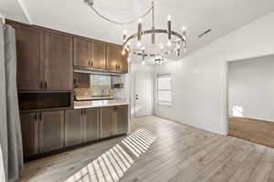Kitchen with dark wood finish cabinetry, light countertops, lofted ceiling, hanging lights, and light wood-style flooring