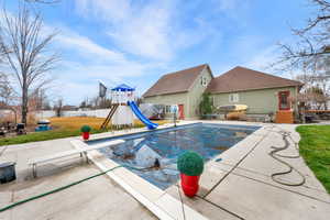 View of pool featuring patio surround, a diving board, a playground, and a water slide