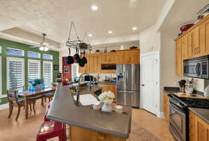 Kitchen with a kitchen island with sink, stainless steel appliances, a ceiling fan, light wood finished floors, and a breakfast bar