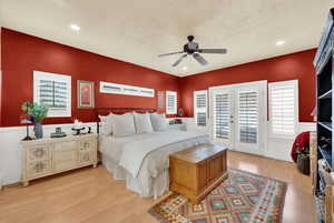 Bedroom with wainscoting, light wood-style flooring, access to outside, ceiling fan, and french doors