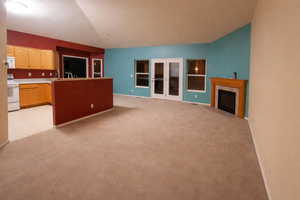 Unfurnished living room featuring lofted ceiling, light carpet, and a fireplace with flush hearth