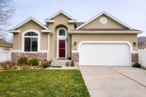 View of front of house featuring an attached garage, stucco siding, driveway, and brick siding