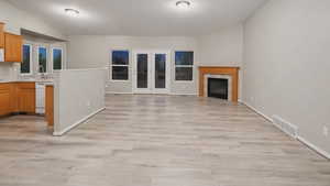 Unfurnished living room with light wood-style floors, a fireplace, vaulted ceiling, and french doors