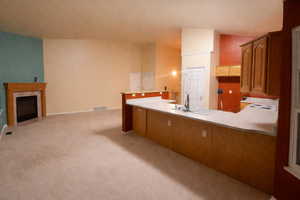 Kitchen featuring light countertops, a peninsula, a fireplace with flush hearth, wood finish cabinetry, and light colored carpet