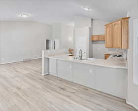 Kitchen featuring light countertops, a peninsula, light wood-type flooring, white range with electric cooktop, and vaulted ceiling