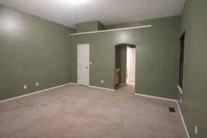 Unfurnished bedroom featuring arched walkways, light carpet, and ensuite bath