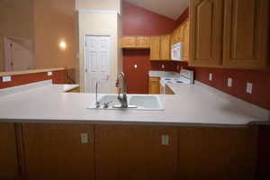 Kitchen with vaulted ceiling, white appliances, light countertops, and a peninsula