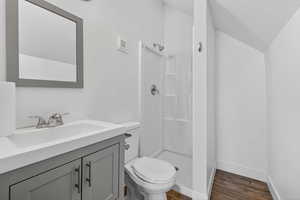 Full bathroom with vanity, a shower stall, dark wood-style floors, and vaulted ceiling