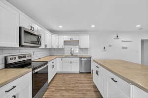 Kitchen with stainless steel appliances, light wood finished floors, white cabinets, butcher block counters, and backsplash