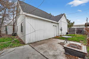 View of side of property with roof with shingles, a fire pit, and a patio