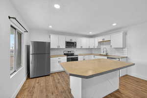 Kitchen with a center island, stainless steel appliances, white cabinetry, tasteful backsplash, and light wood-style floors