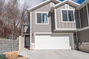 View of front of house with board and batten siding, an attached garage, concrete driveway, and stone siding