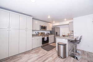 Kitchen with stainless steel appliances, a peninsula, a kitchen breakfast bar, light wood-style floors, and light stone countertops