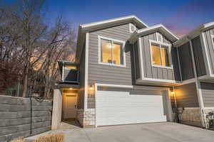 View of front of house with stone siding, a garage, board and batten siding, and driveway