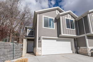 View of front of home with stone siding, an attached garage, board and batten siding, and concrete driveway