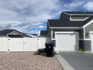View of side of home with a gate, a shingled roof, an attached garage, board and batten siding, and concrete driveway