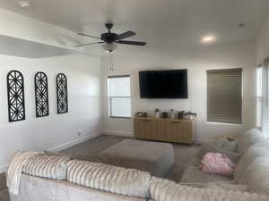 Carpeted living room featuring ceiling fan and baseboards