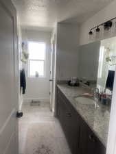 Bathroom with a textured ceiling, vanity, and light tile patterned floors