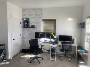 Office with light colored carpet, plenty of natural light, and brick wall