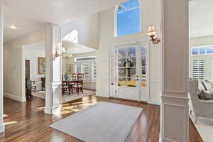 Foyer with dark wood-type flooring, healthy amount of natural light, decorative columns, and a high ceiling