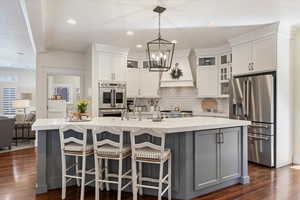 Kitchen with stainless steel appliances, glass fronted cabinets, dark wood-style flooring, a breakfast bar area, and two tone color scheme