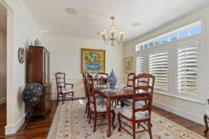 Dining space with ornamental molding, suspended lighting, and dark wood-type flooring