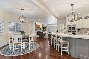 Dining room featuring suspended lighting, a warm lit fireplace, dark wood-style floors, and ornamental molding
