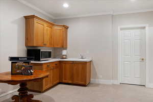 Bar area featuring light countertops, stainless steel microwave, crown molding, wood finish cabinets, and light carpet