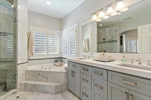 Full bath with double vanity, a marble finish shower, a garden tub, light marble finish flooring, and recessed lighting