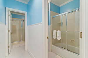 Full bath featuring wainscoting, crown molding, enclosed tub / shower combo, and light tile patterned floors