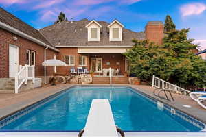 Back of house at dusk featuring a patio, an outdoor pool, and brick siding