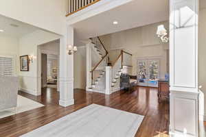 Foyer entrance featuring decorative columns, dark wood-style floors, french doors, a high ceiling, and suspended lighting