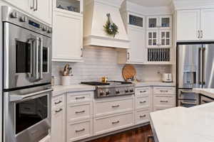 Kitchen featuring stainless steel appliances, glass insert cabinets, white cabinets, and dark wood-style flooring