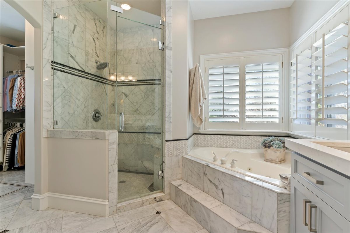 Bathroom with a marble finish shower, a walk in closet, a jetted tub, and vanity