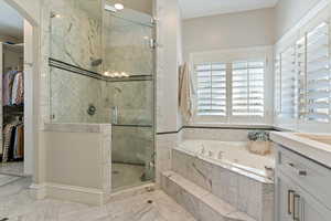 Bathroom with a marble finish shower, a walk in closet, a jetted tub, and vanity