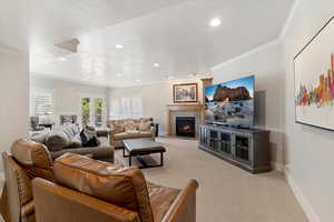 Living area featuring light carpet, a fireplace with flush hearth, crown molding, and recessed lighting