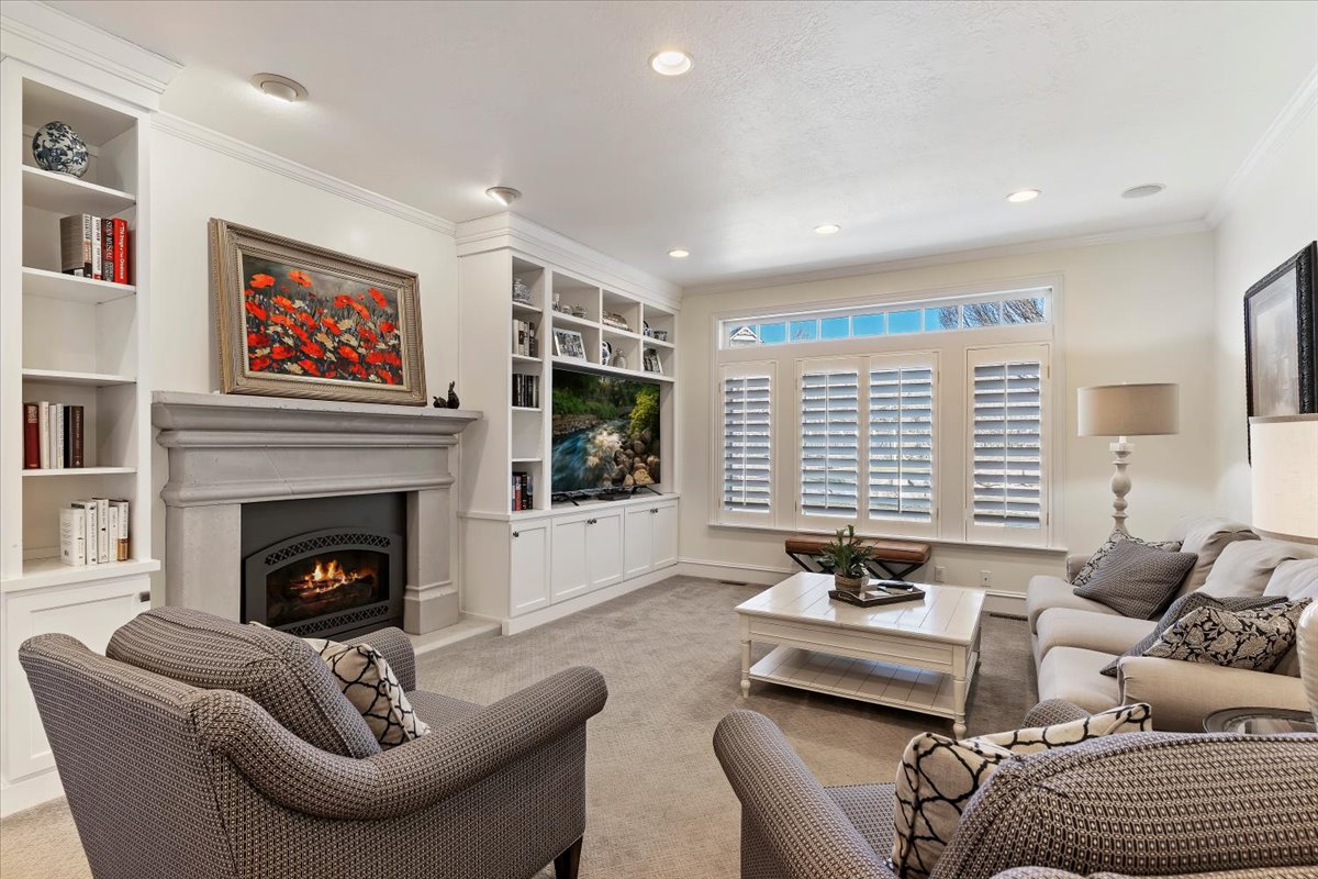 Living room featuring built in shelves, ornamental molding, light carpet, a warm lit fireplace, and recessed lighting