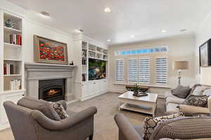 Living room featuring built in shelves, ornamental molding, light carpet, a warm lit fireplace, and recessed lighting