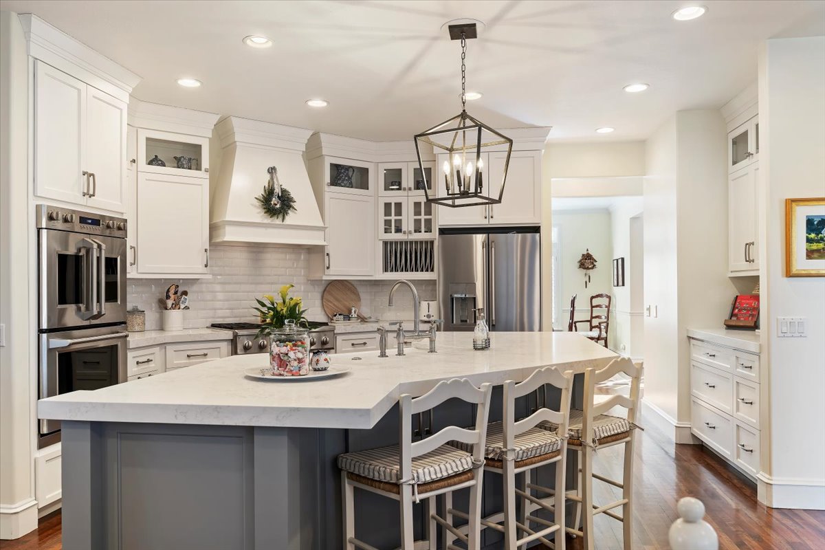 Two tone kitchen with glass fronted cabinets, stainless steel appliances, dark wood finished floors, an island with sink, and dual tone cabinetry