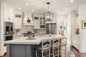 Two tone kitchen with glass fronted cabinets, stainless steel appliances, dark wood finished floors, an island with sink, and dual tone cabinetry
