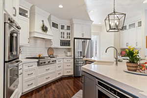 Two tone kitchen with glass fronted cabinets, stainless steel appliances, light stone countertops, dark wood-style flooring, and dual tone cabinetry