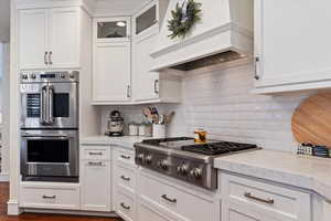 Kitchen with stainless steel appliances, glass fronted cabinets, and white cabinets