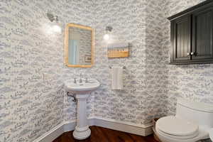Half bath featuring dark wood finished floors and wallpapered walls