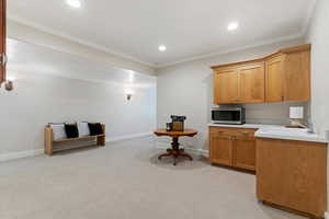 Kitchen with light countertops, stainless steel microwave, crown molding, recessed lighting, and wood finish cabinetry